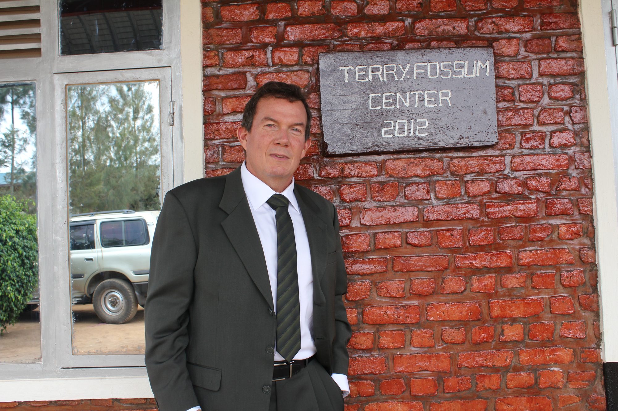 Terry L. Fossum in a suit beside the Terry Fossum Center 2012 plaque on a brick building in Rwanda