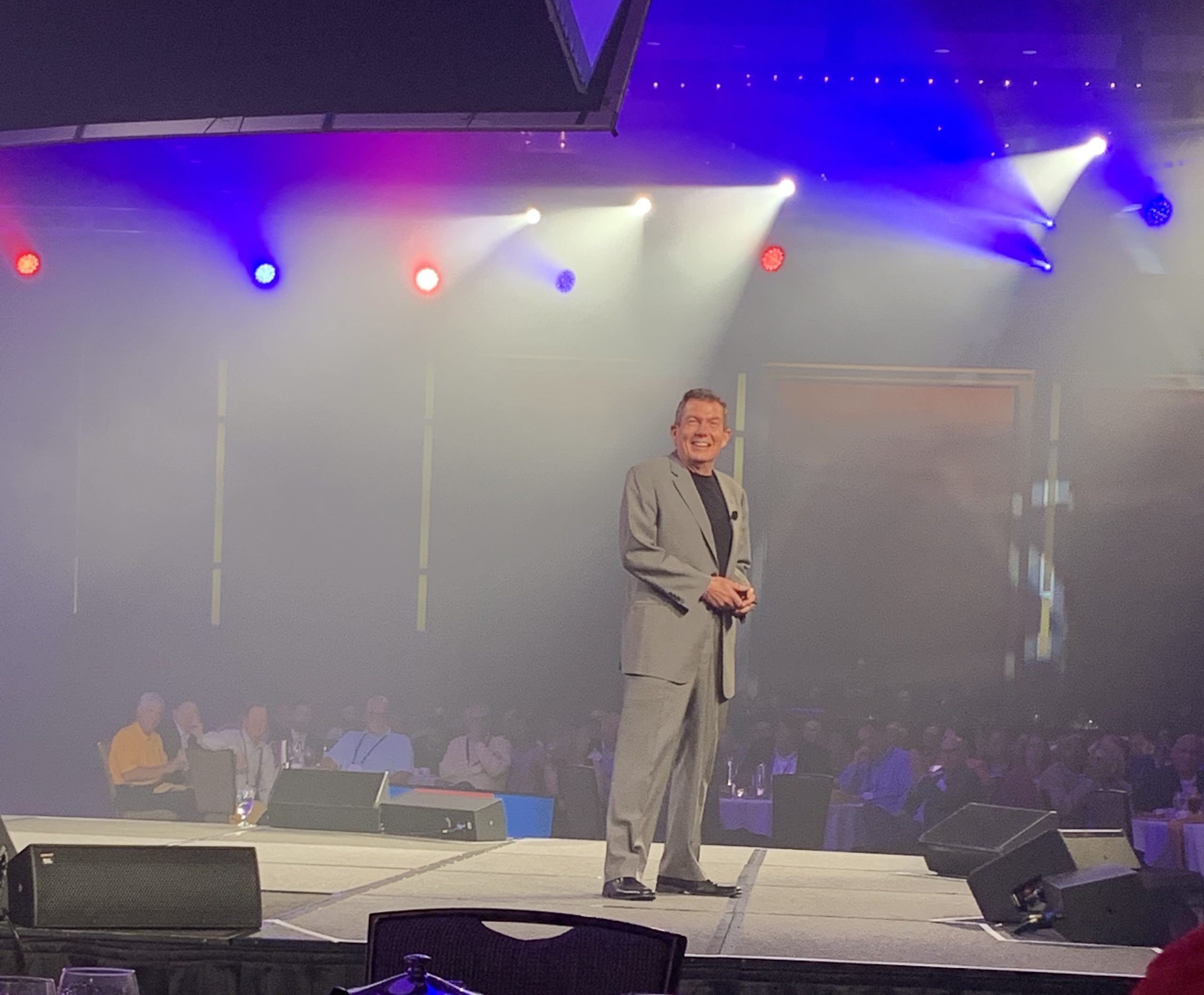 Terry L. Fossum on a big conference stage, stage lights blazing behind him, a full house in front