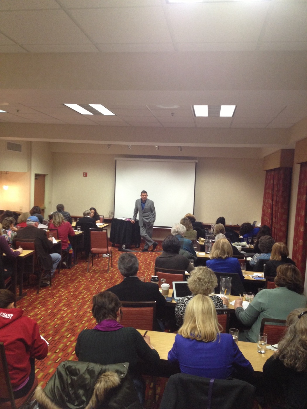 Terry L. Fossum teaching a small workshop room, leaning against the table at the front while the group works