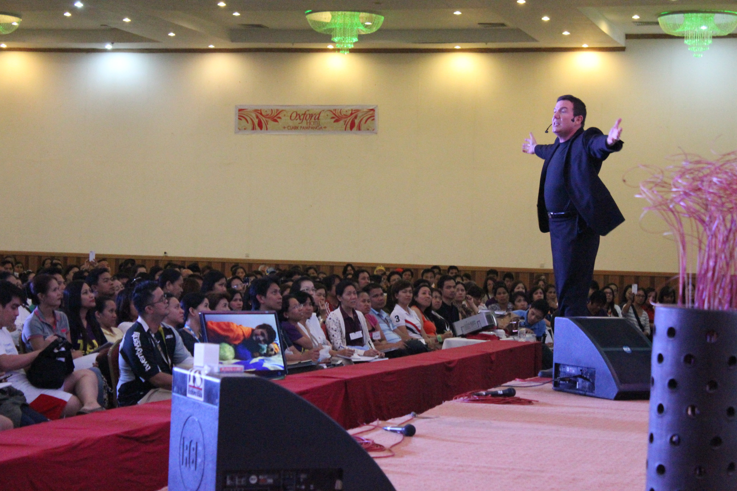 Terry L. Fossum on stage with arms wide, audience visible in front of him